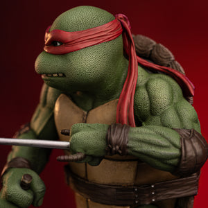 Profile close-up of Raphael's muscular arm, leather elbow pad, and hand gripping a metallic sai dagger on the Iron Studios collectible.