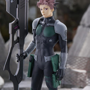 Medium close-up shot of the Gen Narumi anime figure positioned in a ruined urban battlefield setting, emphasizing the detailed tactical suit.