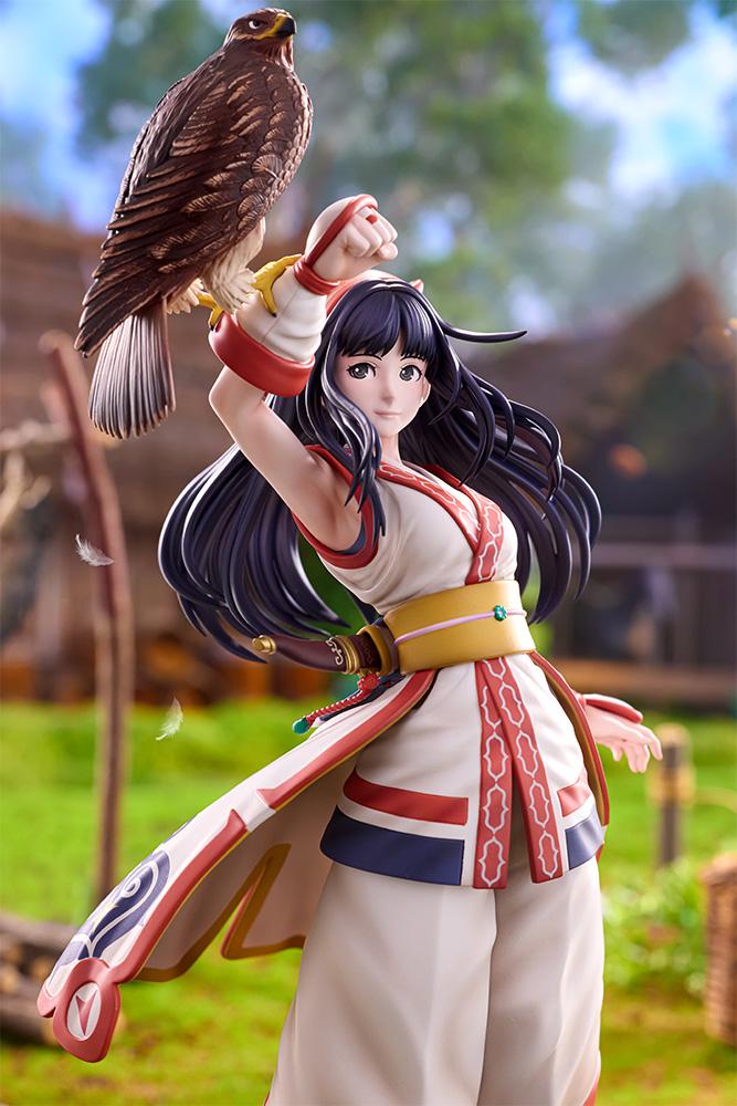 Close-up view of Nakoruru figure with floating feathers against a lush green outdoor village backdrop