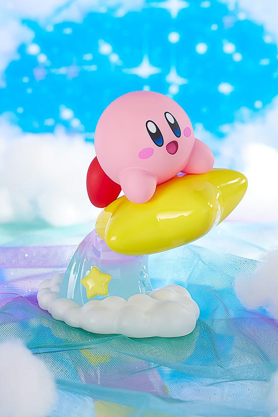 Whimsical diorama display of the Kirby figure riding his star over light clouds against a vibrant, glittering blue sky background.
