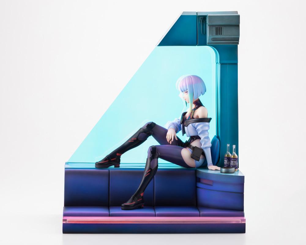 Front side view of Lucy figure seated on blue room diorama sofa showing signature outfit and Broseph bottles.