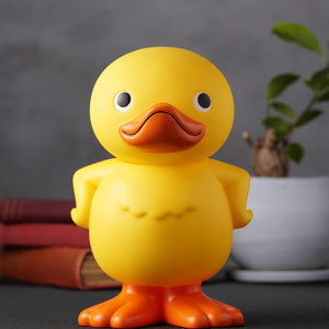 Front view of the GA-KO soft vinyl duck coin bank arranged on a desk display with books and houseplant.