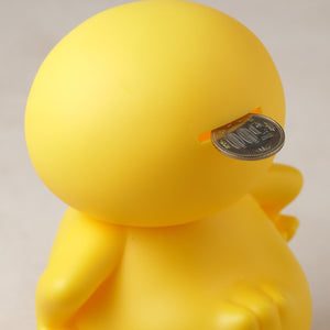 Close-up shot of a coin being inserted into the slot on the back of the GA-KO duck vinyl coin bank.