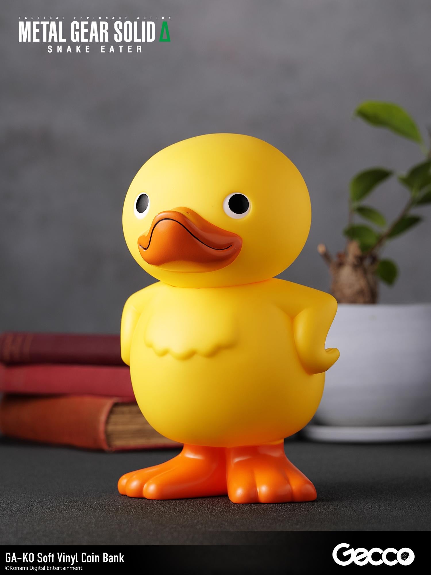 Three-quarter left angle shot of the GA-KO duck vinyl bank on a lifestyle desk setup.
