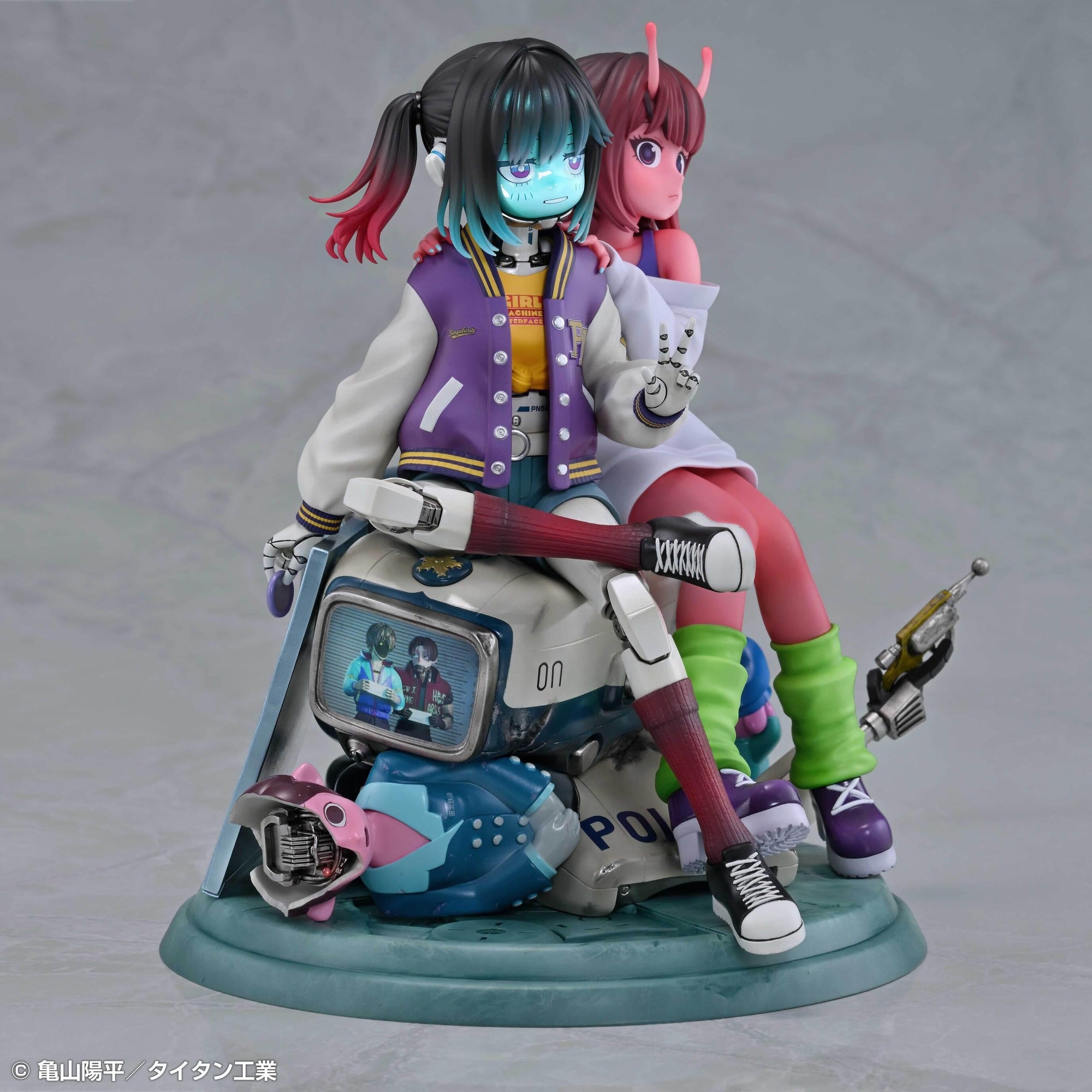 Three-quarter front-left angle of the Chiharu and Makina figure showing the detailed jacket text and damaged monitor details on the base.