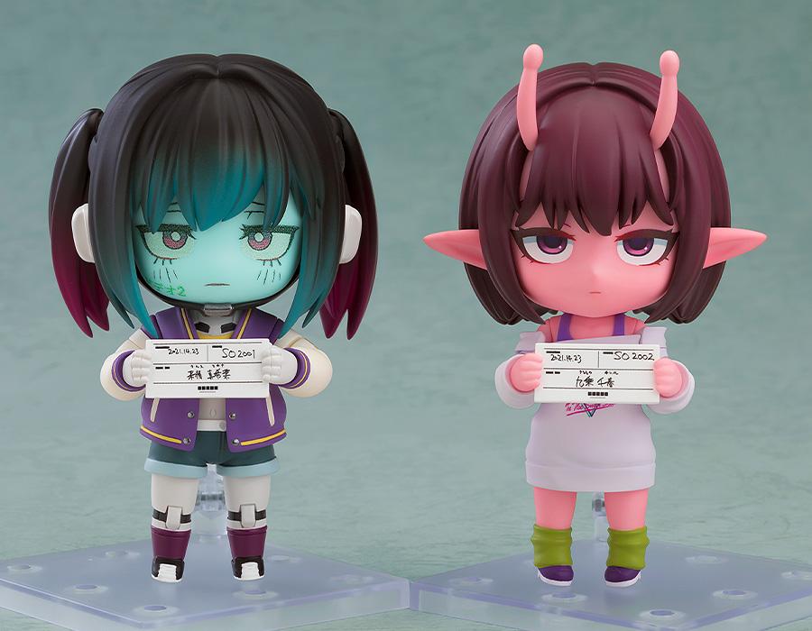 Comparison shot featuring Makina and Chiharu Nendoroids side-by-side holding their respective mugshot papers.