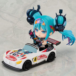 An action shot showing the Nendoroid Racing Miku: 2026 Ver. figure seated in and driving the included Nendoroid car on a racetrack, smiling and waving.