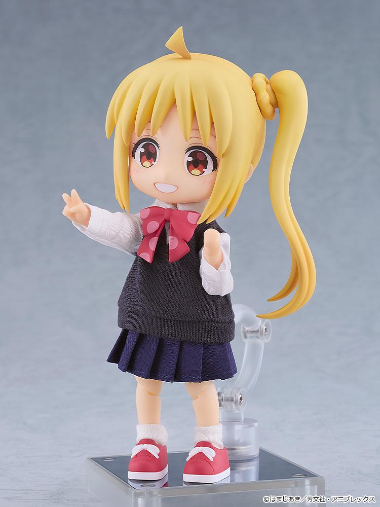 Three-quarter view of the Nijika Ijichi Nendoroid Doll figure mounted on its magnetic stand, showcasing the detailed fabric school uniform vest, pleated skirt, and pink polka-dot bow.