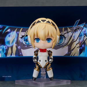 Nendoroid Aigis 2.0 figure posed frontally against a background panel of her character from the Persona 3 Reload game.
