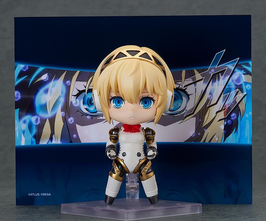 Nendoroid Aigis 2.0 figure posed frontally against a background panel of her character from the Persona 3 Reload game.