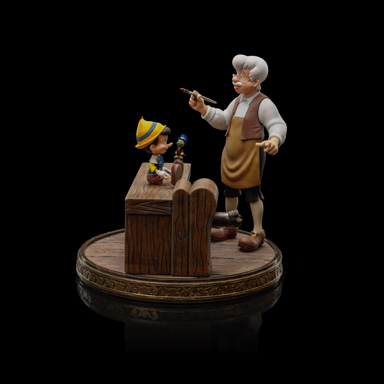 A front view of the Pinocchio and Geppetto Art Scale 1/10 statue by Iron Studios, showing Jiminy Cricket on Pinocchio’s foot on the workbench.
