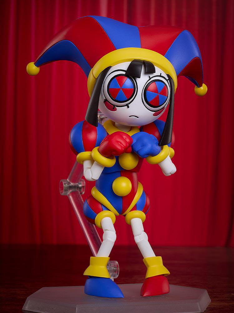 Highly articulated Pomni figma figure showing her frightened face plate with pinwheel eyes, clenching her gloved fists nervously against a deep red velvet curtain backdrop.