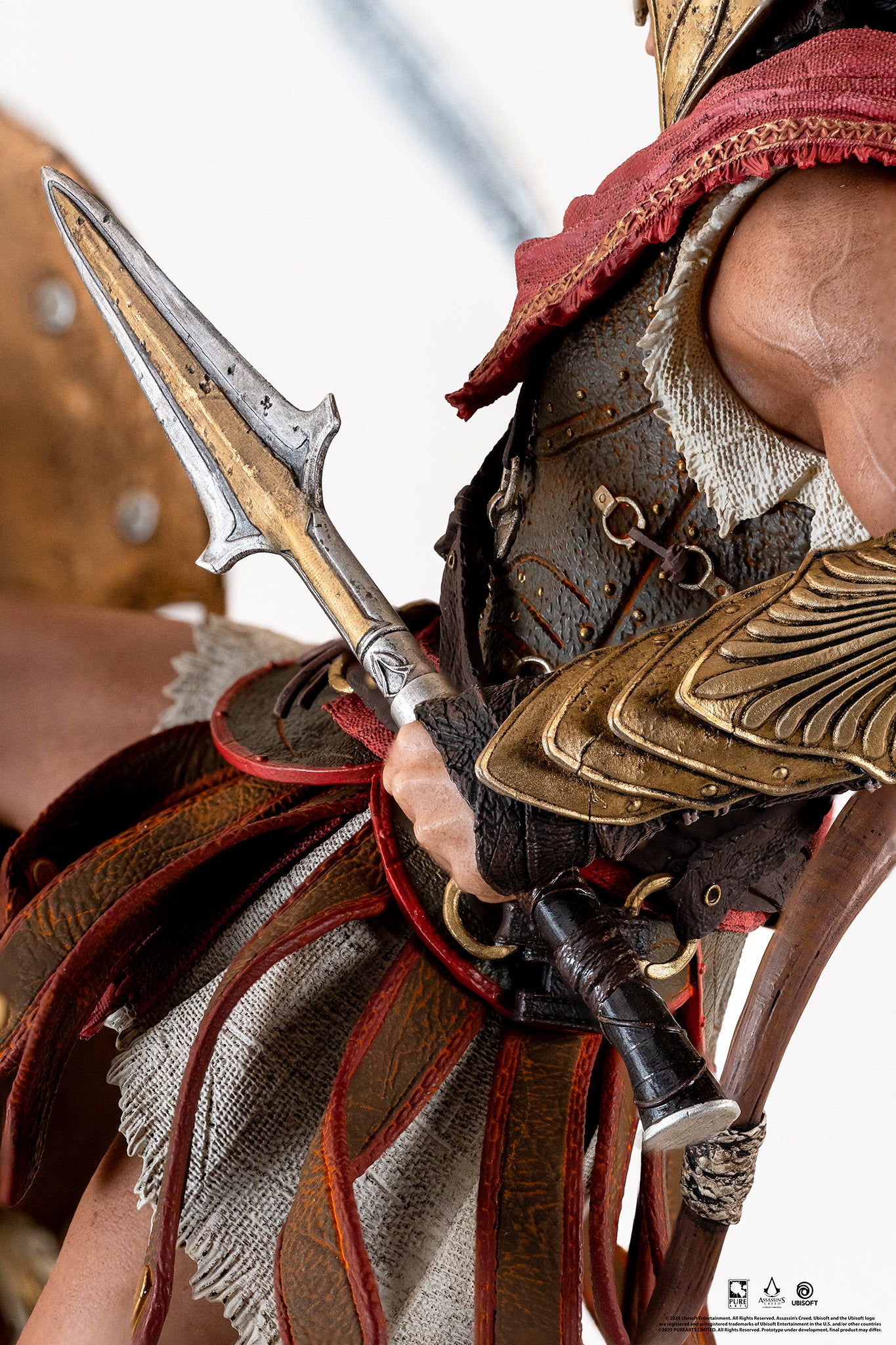 Close-up on Alexios' hand gripping the broken spear, detailing his golden forearm armor and leather skirt (pteruges).