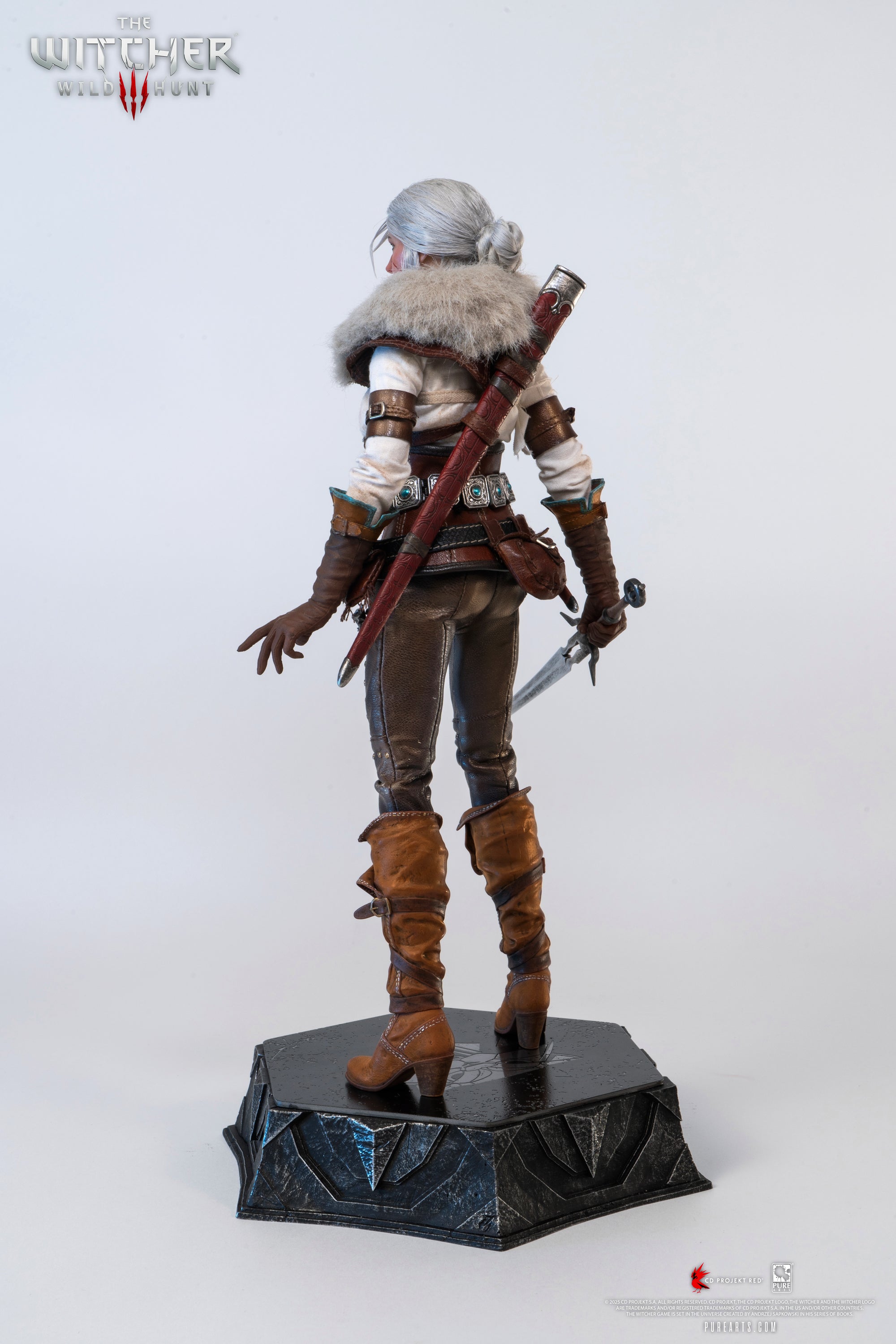 Rear view of the Ciri figure wearing the fur mantle, with her hand resting on the dagger's hilt.