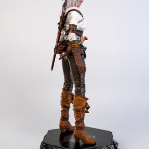 A straight side view of the Ciri figure, emphasizing the layers of her clothing and the Witcher wolf medallion on the base.