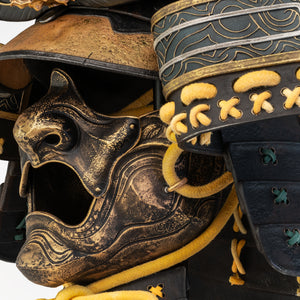 Detailed close-up of the left side of the PureArts Yasuke helmet's mask, showcasing the textured gold finish, rope ties, and the layered armor plates of the neck guard.