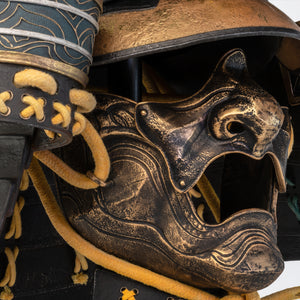 Profile view of the PureArts Yasuke helmet showing the weathered gold and black facemask (mempo) with intricate details and a stylized, open mouth.
