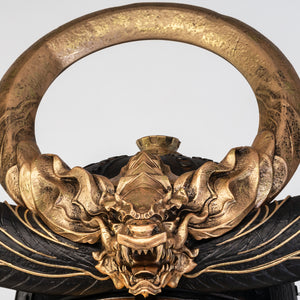 A close-up view of the intricate gold crest on the PureArts Yasuke helmet replica, featuring a detailed, fierce dragon and a prominent circular ring.