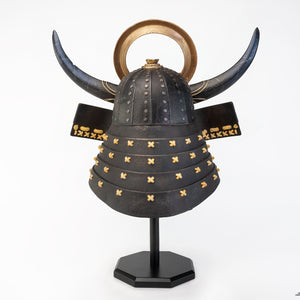 Back view of the complete PureArts Yasuke helmet replica on its display stand, showcasing the black horns, gold crest, and the studded helmet design.







