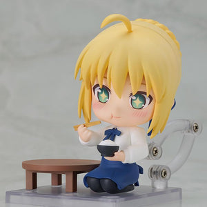Saber Casual Outfit Version Nendoroid figure kneeling beside a low dining table, holding a rice bowl and chopsticks with a delighted, sparkling-eye face plate.