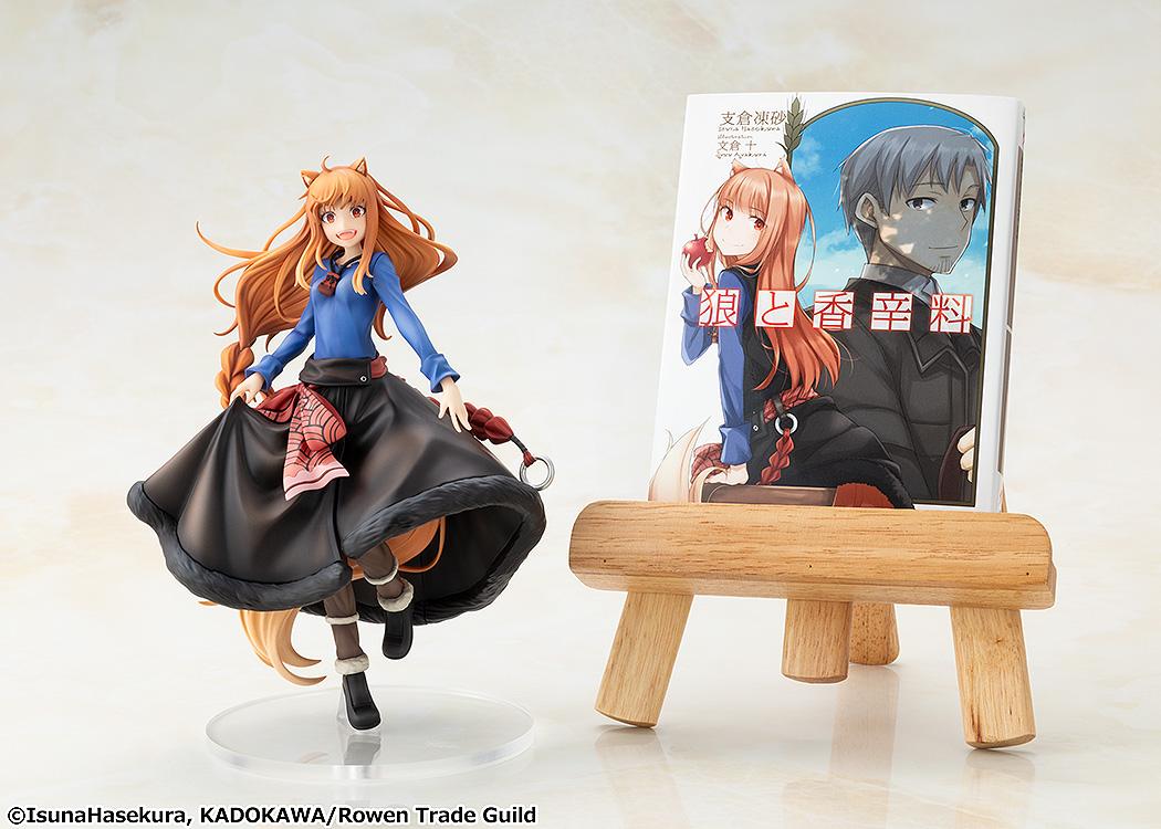 The KD Colle Holo figure displayed beside a Spice and Wolf light novel volume resting on a mini wooden easel stand.