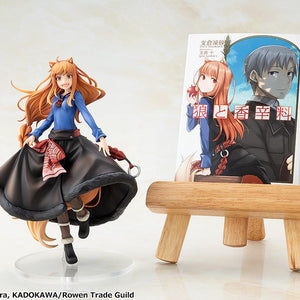 The KD Colle Holo figure displayed beside a Spice and Wolf light novel volume resting on a mini wooden easel stand.