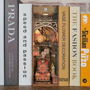 The assembled "The Steam Age" book nook seamlessly integrated onto a bookshelf between various large books, showing the warm LED lighting.