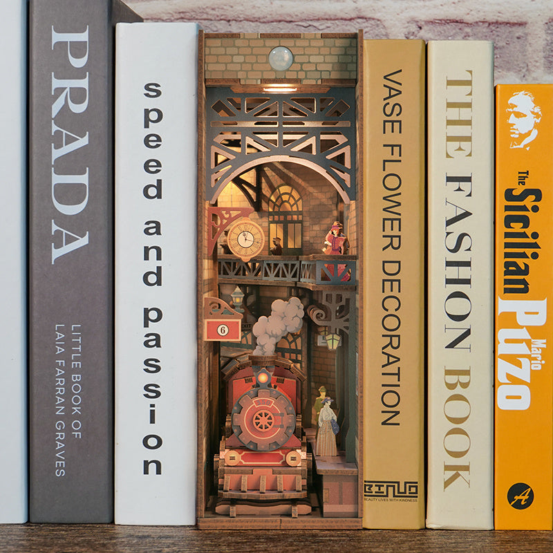 The assembled "The Steam Age" book nook seamlessly integrated onto a bookshelf between various large books, showing the warm LED lighting.