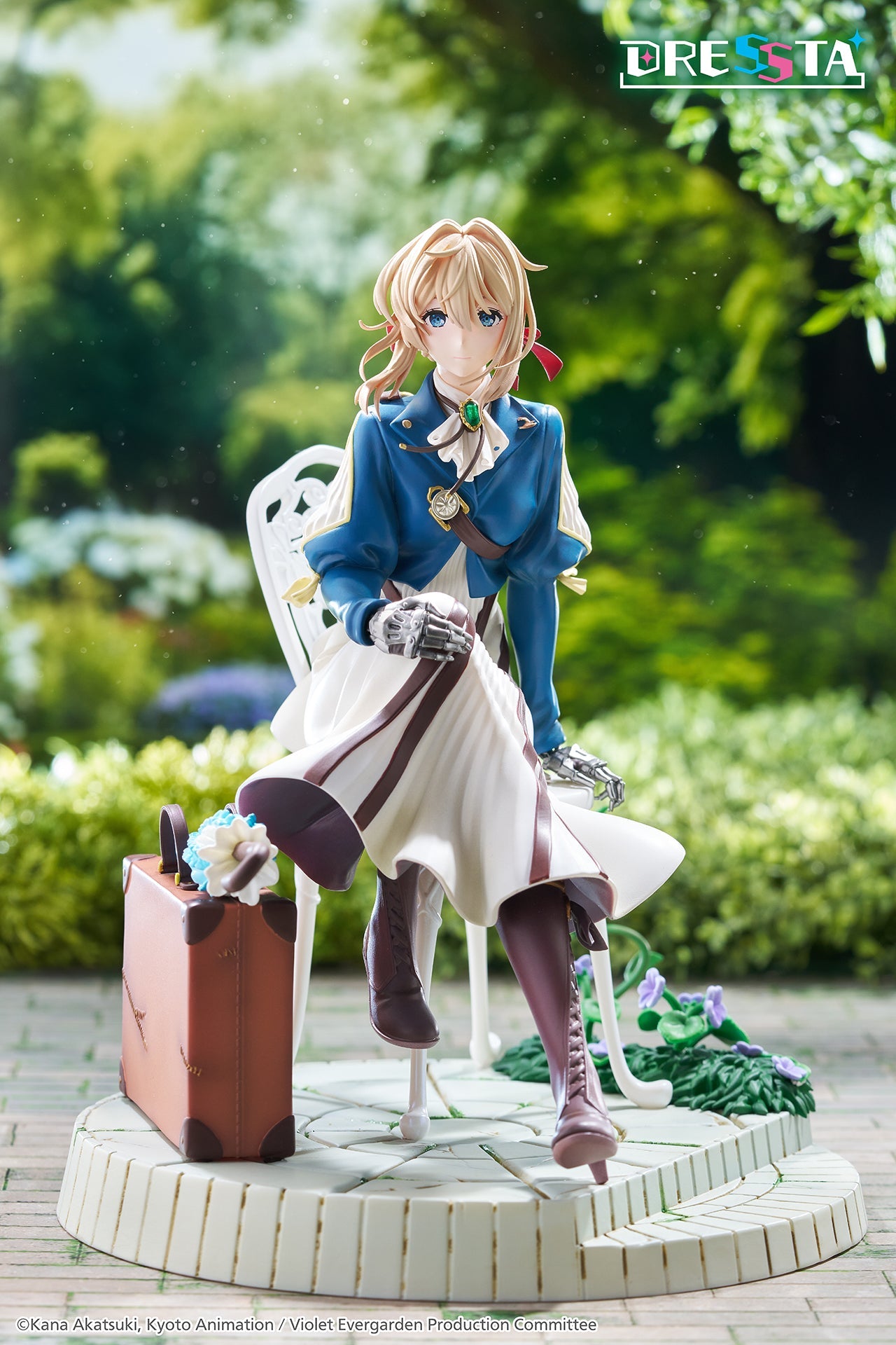 Outdoor garden diorama display of Violet Evergarden DRESSTA statue sitting on a paved patio chair surrounded by green foliage