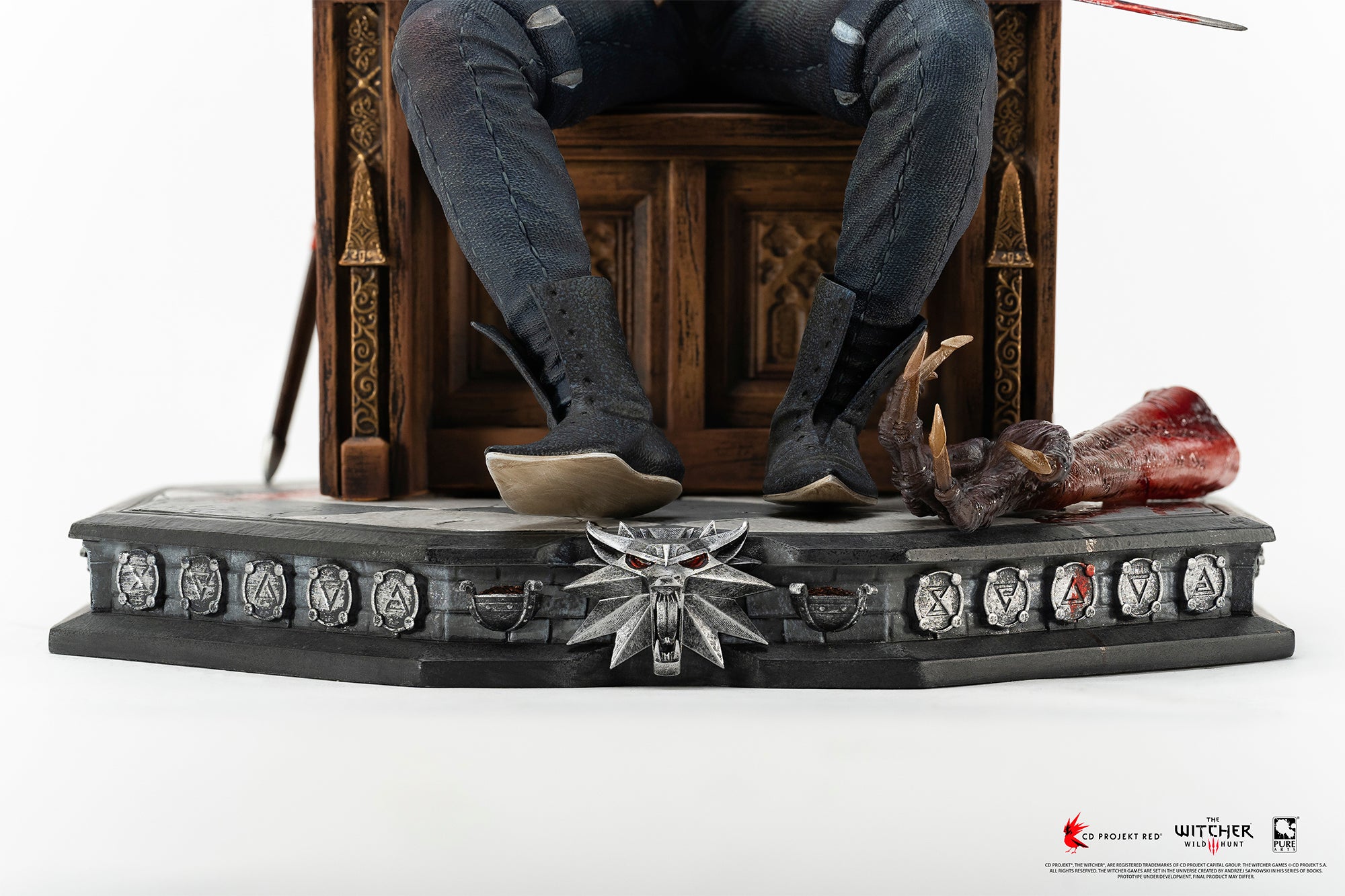 Low-angle view of Geralt's boots rested on the stone base next to Dettlaff's severed vampire arm and the wolf medallion base ornament.