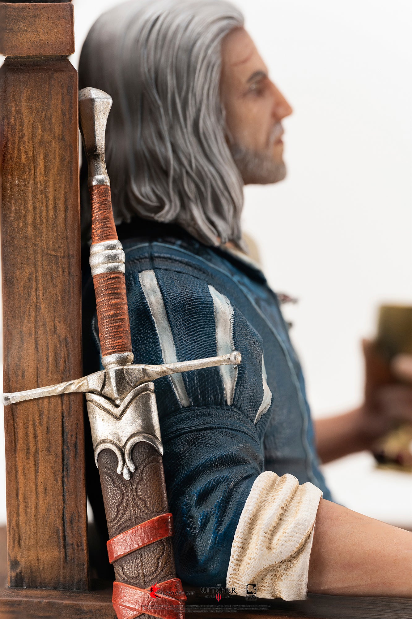 Side detail shot showing Geralt's steel sword in its leather scabbard resting against the side of the wooden throne.