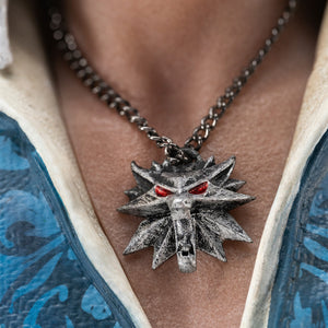 Detailed close-up shot of Geralt of Rivia's silver Wolf School medallion with glowing red eyes.